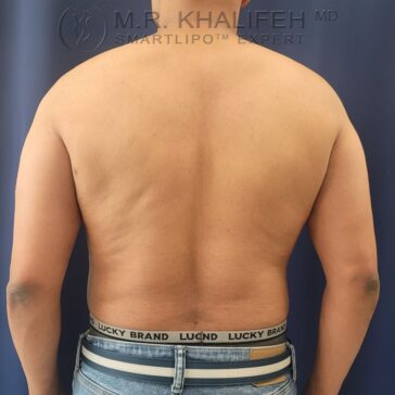 A person stands with their bare back facing the camera, wearing jeans and underwear labeled "Lucky Brand" against a plain dark background.