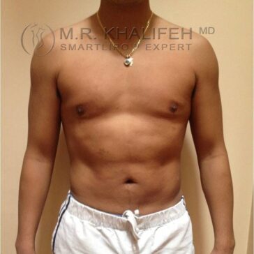 A shirtless person stands facing forward, wearing a necklace and white shorts with a stripe, against a plain beige background.
