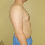 A shirtless person in blue pants is standing sideways against a plain yellow wall.