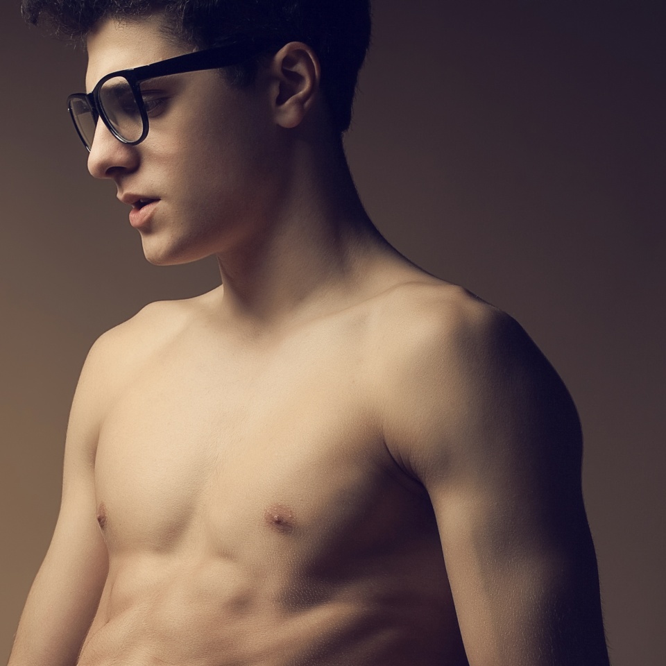Male beauty concept. Portrait of fashionable young man with stylish haircut wearing trendy glasses, posing over brown background. Perfect hair, skin. Hipster style. Close up. Copy-space. Studio shot