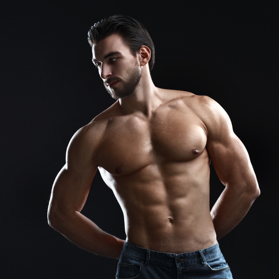 Young athletic man with a naked torso isolated on a black background.
