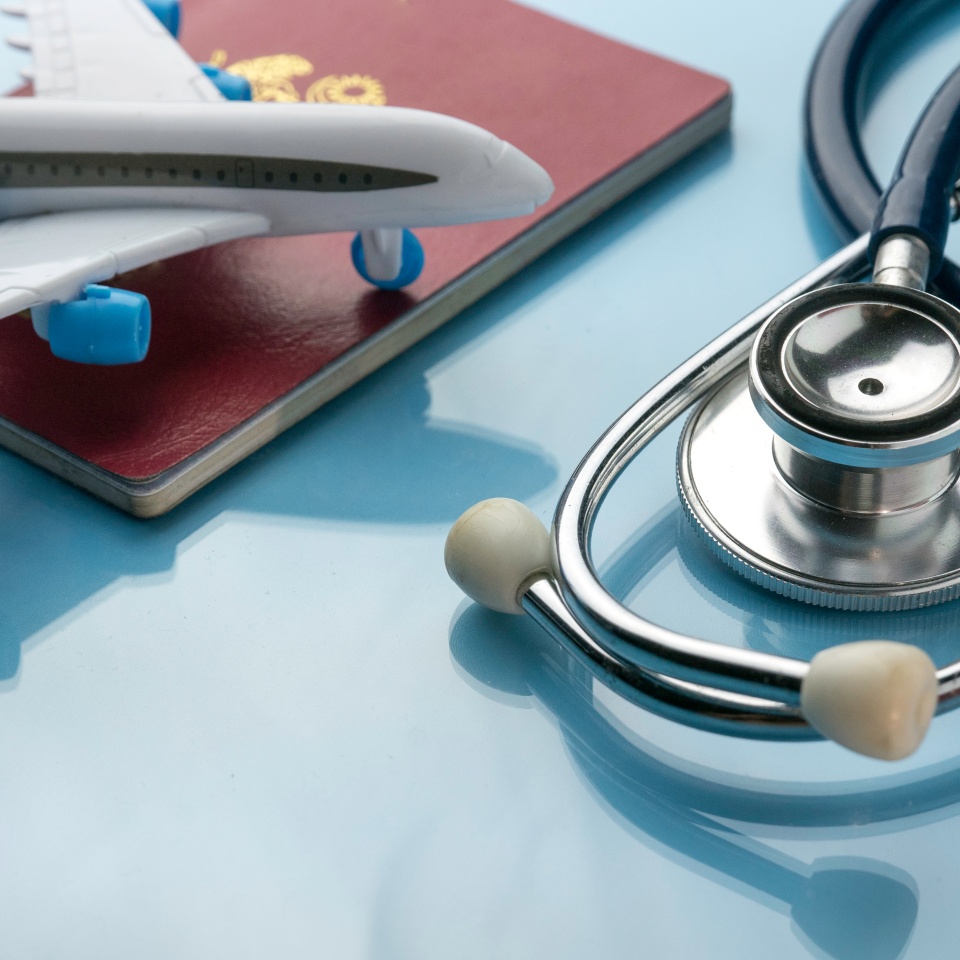 Healthcare,transportation and tourism concept with stethoscope, passport and plane model on a blue glass background.