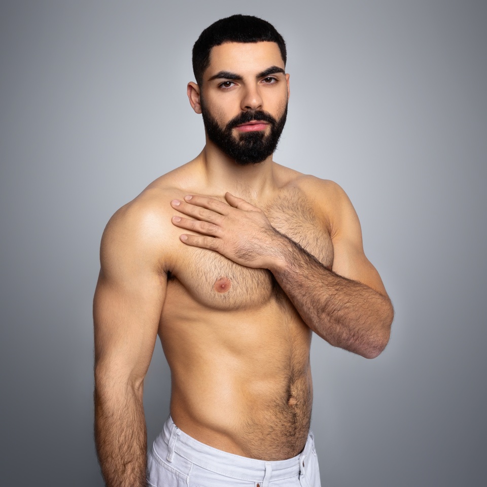 Sexy topless middle eastern young man shirtless looking at camera, taking care of his body, touching his chest, skincare after shower, isolated in grey background, copy space