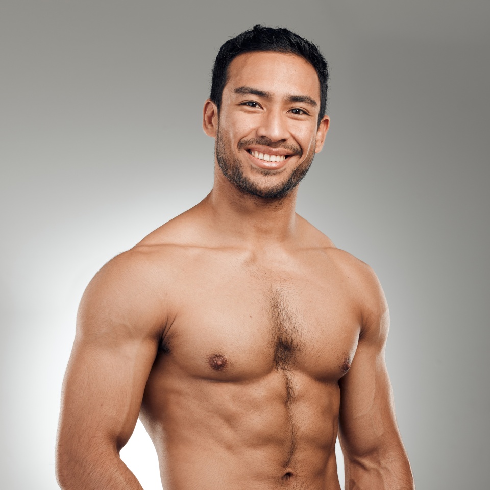 Man, portrait and smiling in studio with abs or muscles, shirtless and grey background with model or bodybuilder. Jeans, strong chest and Asian male person on backdrop, confidence with six pack