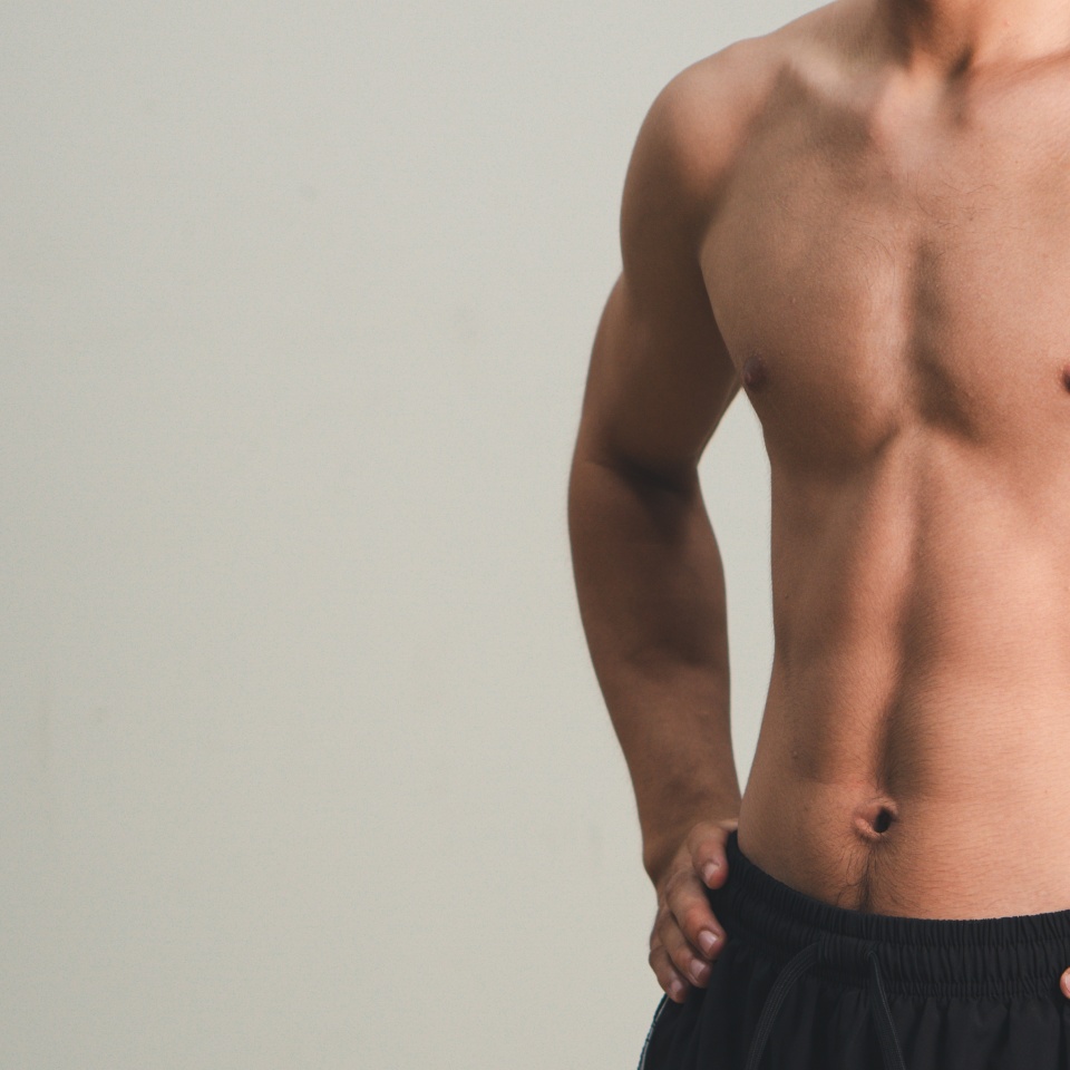 Handsome muscular young man posing against a grey background. male model taking off his shirt on a gray background, body transformation , weight loss, sixpack