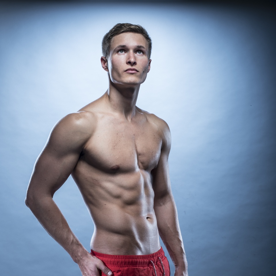 blonde Male fitness model wearing red shorts on blue
