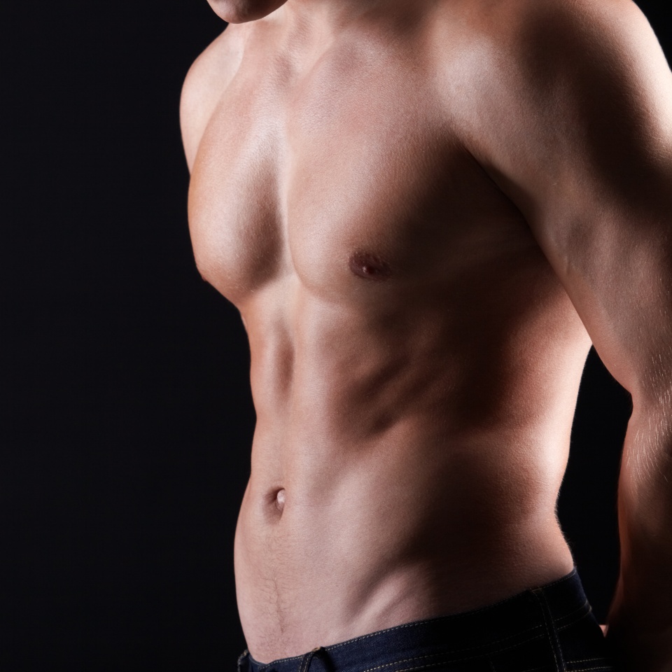Torso of strong man in jeans against dark background